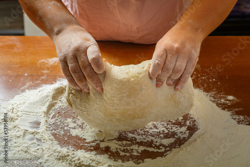 The hands of a Jewish woman knead the dough for challah for a festive meal on Shabbat on a wooden table.