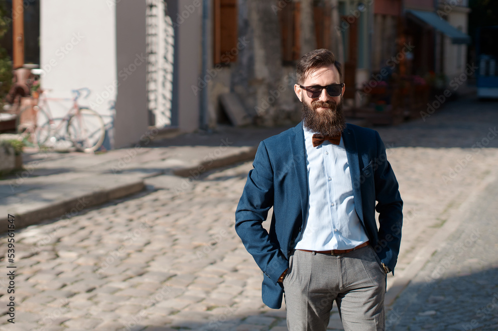 Stylish man with beard wearing a jacket, shirt and bow tie with hands in pockets