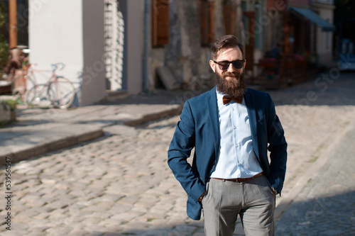 Obraz na płótnie Stylish man with beard wearing a jacket, shirt and bow tie with hands in pockets w salonie