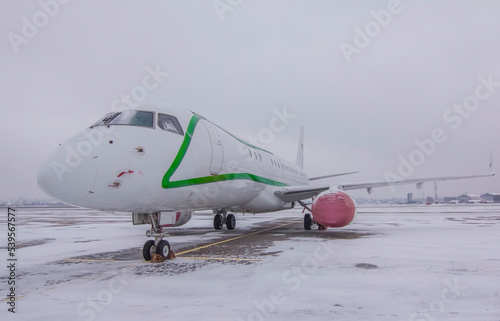 A jet passenger plane stands parked at the airport with covers put on engines in winter against a cloudy sky