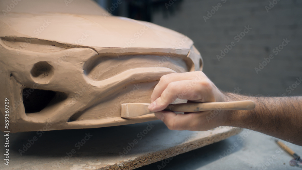 Hands of a male designer works on the sculpture of a car using sculpting tools. Smooths out the surface of the unfinished model in a workshop. Automotive industry. Hands of a male designer works on the sculpture of a car using sculpting tools. Smooths out the surface of the unfinished model in a workshop. Automotive industry.