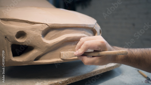 Hands of a male designer works on the sculpture of a car using sculpting tools. Smooths out the surface of the unfinished model in a workshop. Automotive industry.