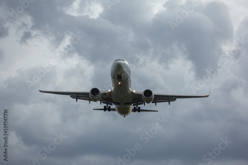 A jet passenger airliner is landing in front of the camera with landing gear extended and flaps extended, against a cloudy sky