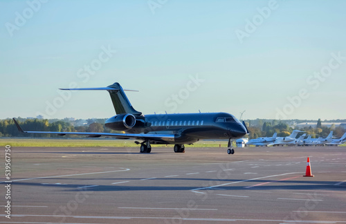 A dark green private business jet is parked at the airport in front of other business jets, no tail numbers
