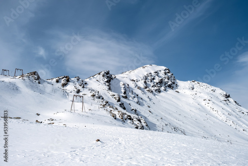 View of the mountain range, steep slopes and snow-capped rocky peaks with supports for the cable car for skiers and tourists. Selective focus.