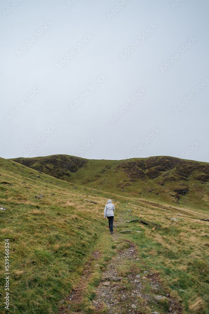 Person walking or hiking in raincoat near to Bowscale Tarn lake in mountains, United Kingdom