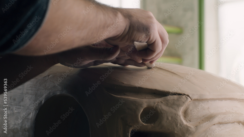 Closeup hands of a car designer works on the design details of an unfinished sculpture of the prototype eco-friendly electric car model. Hand made car sculpture on a wooden table.