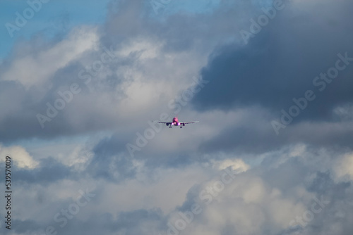A white and pink jet passenger airliner comes in for landing against a clear sky. Low angle photo from the end of the runway