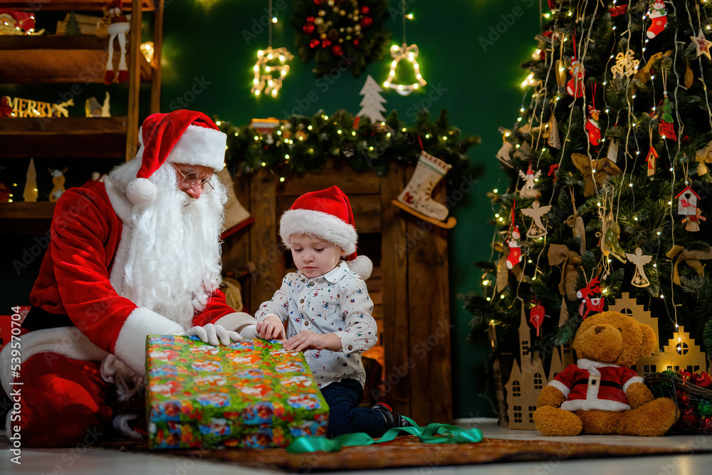 Little boy opening his Christmas gift with Santa Claus. Christmas Scenes. New Year concept 