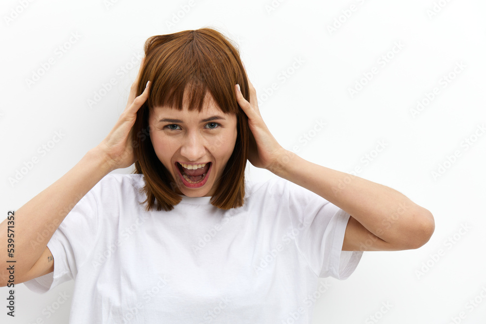 funny, very emotional woman screams loudly clutching her head while standing in a white T-shirt on a light background funny, very emotional woman screams loudly clutching her head while standing in a white T-shirt on a light background