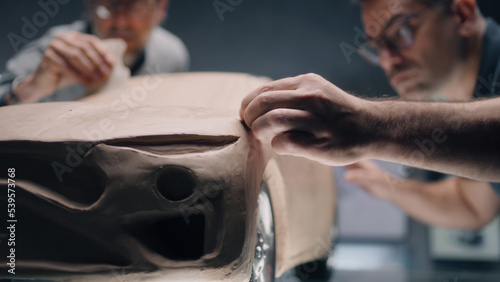 Two male automotive designers creating futuristic plasticine clay prototype of car with professional tools. Future design of new generation electric car. Working in modern car design studio.