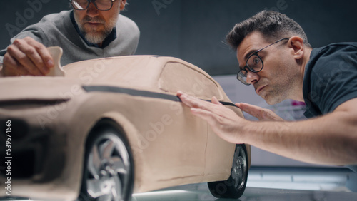 Two male automotive designers creating futuristic plasticine clay prototype of car with professional tools. Future design of new generation electric car. Working in modern car design studio. © Framestock
