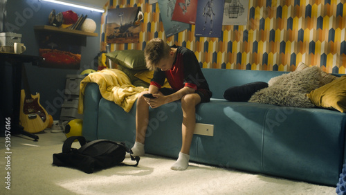 Young boy pratices football in his bedroom. Young enthusiastic soccer player before the match. A modern room with a guitar, posters on the wall and a study table with the lamp. photo