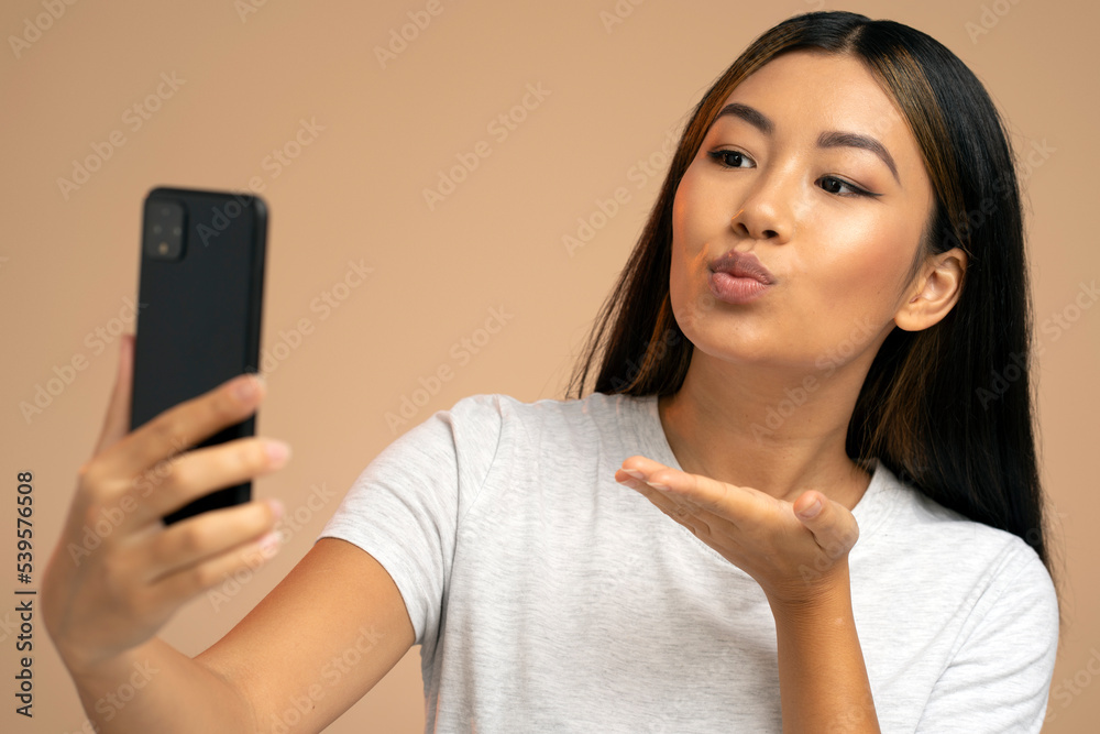 Joyful asian young woman using smartphone for video call sending air kiss to webcam Joyful asian young woman using smartphone for video call sending air kiss to webcam
