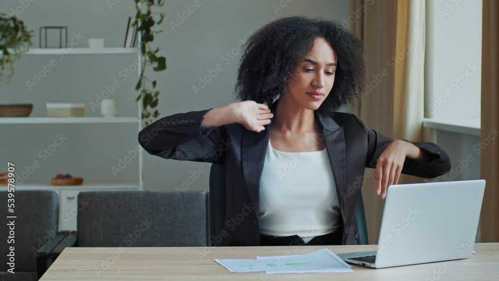 Young ethnic african american woman employee work overtime on computer at office sit in uncomfortable position relieve muscle spasm tension tired overworked female girl massaging back relax gymnastic Young ethnic african american woman employee work overtime on computer at office sit in uncomfortable position relieve muscle spasm tension tired overworked female girl massaging back relax gymnastic