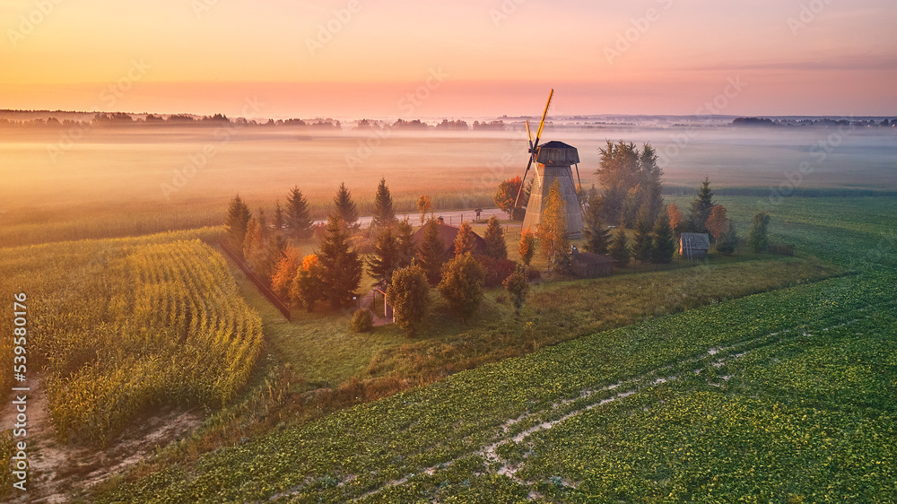 Traditional Wooden Windmill Morning Landscape. Rural colorful Sunrise, Foggy green fields. Dudutki village