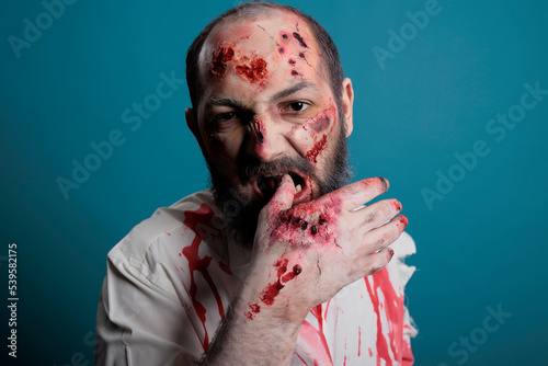 Crazy halloween zombie biting bloody hand with scars and wounds, being aggressive and dangerous. Undead evil monster with apocalyptic demon look and scary face, cruel wounded corpse.
