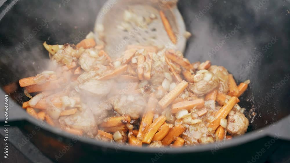 Close-up of a slotted spoon stirring meat, carrots and onions. Roasted in a cauldron. Steam rises from food. Close-up of a slotted spoon stirring meat, carrots and onions. Roasted in a cauldron. Steam rises from food.