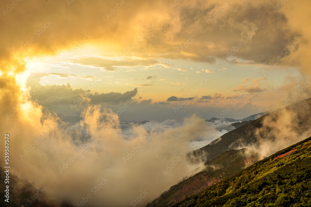 夕焼けと霧に巻かれる北アルプスの写真（長野県）