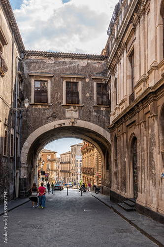 Beautiful street with historic buildings and a stone arch in Catania