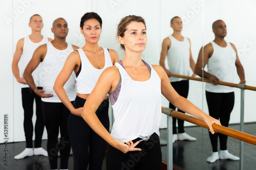 Adult women and men doing exercises on stretching ballet barre