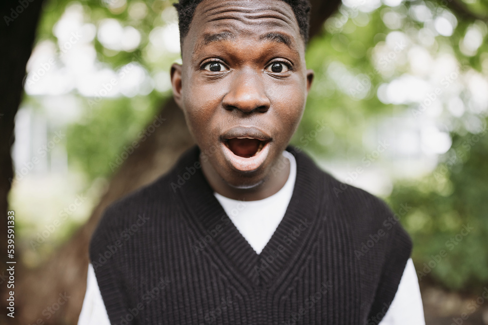Shocked surprised young African man in park. Fall or spring season Shocked surprised young African man in park. Fall or spring season