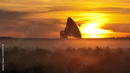 Aerial view. A giant radio telescope for space exploration in a foggy forest during a bloody dawn. Mysterious haze over the forest the sun's rays of dawn break through the red clouds. photo