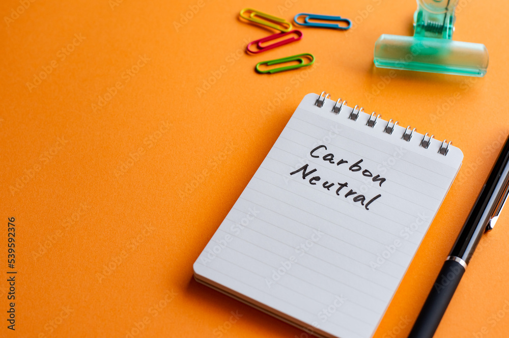 There is a notebook with the word carbon neutral. It's placed on a color background. There is a notebook with the word carbon neutral. It's placed on a color background.