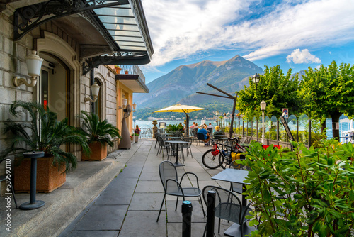 Tourists dine at a waterfront outdoor cafe along the shores of Lake Como at summer in the picturesque town of Bellagio, Italy.