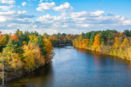 Fototapeta Naklejka Na Ścianę i Meble -  vibrant colors of October. wide panoramic view of a beautiful serenity yellow-orange autumn morning park with lush trees reflected in the river water. picturesque fall landscape