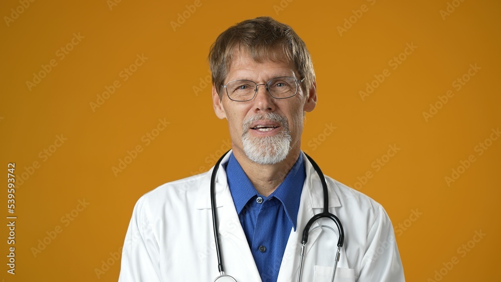 Portrait of tired handsome doctor man in professional medical white coat is isolated on solid yellow studio background. Bored doctor with beard and stethoscope Portrait of tired handsome doctor man in professional medical white coat is isolated on solid yellow studio background. Bored doctor with beard and stethoscope