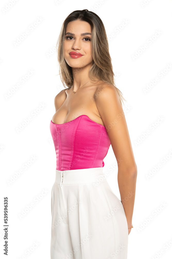 young modern smiling woman in white pants and pink corset posing on white background