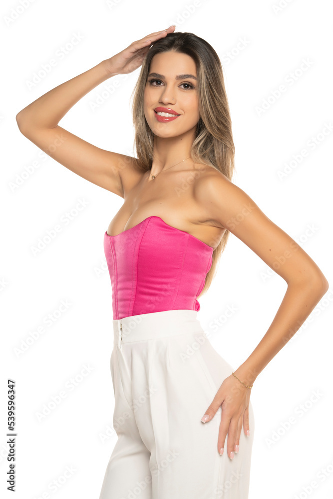 young modern smiling woman in white pants and pink corset posing on white background young modern smiling woman in white pants and pink corset posing on white background