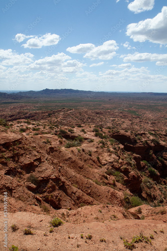 The steep canyon. Panorama view of the red desert, cliffs, orange sandstone formations and rocky mountains in the horizon in Sierra de las Quijadas national park in San Luis, Argentina. The steep canyon. Panorama view of the red desert, cliffs, orange sandstone formations and rocky mountains in the horizon in Sierra de las Quijadas national park in San Luis, Argentina.