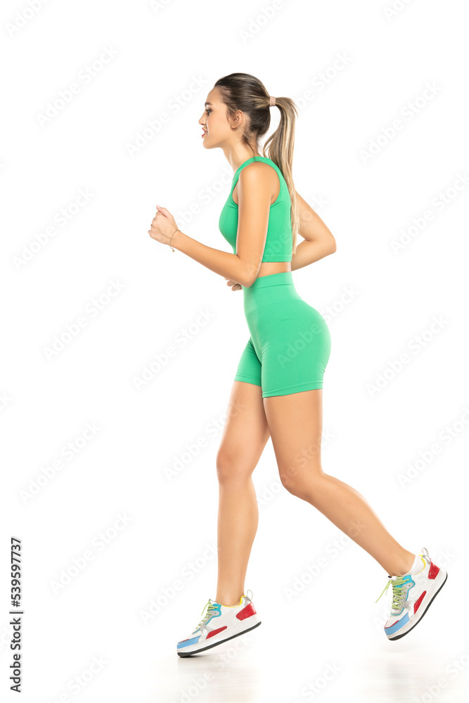young sporty smiling woman in green shorts and top running on white background young sporty smiling woman in green shorts and top running on white background