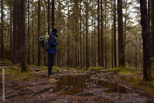 A male hiker with a backpack standing on a wet muddy path in the forest.