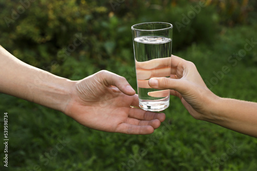 Woman giving glass of fresh water to man outdoors, closeup
