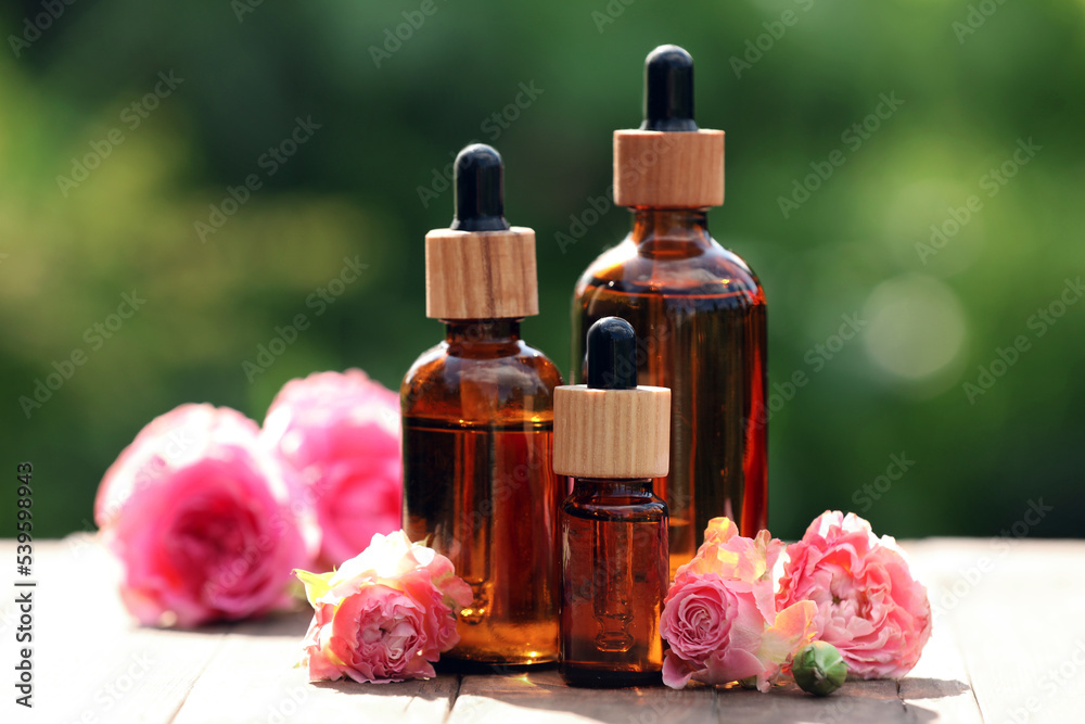 Bottles of rose essential oil and flowers on wooden table outdoors Bottles of rose essential oil and flowers on wooden table outdoors
