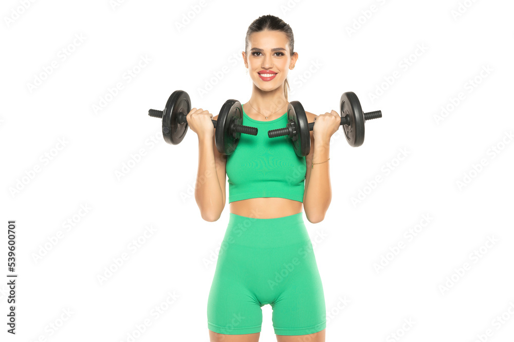 young sporty smiling woman in green shorts and top holding weights on white background young sporty smiling woman in green shorts and top holding weights on white background