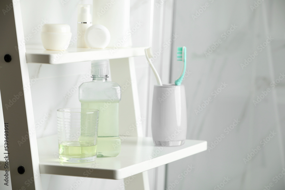 Bottle and glass with mouthwash on white shelf indoors, space for text Bottle and glass with mouthwash on white shelf indoors, space for text