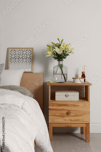 Vase with bouquet of fresh flowers on wooden nightstand in bedroom