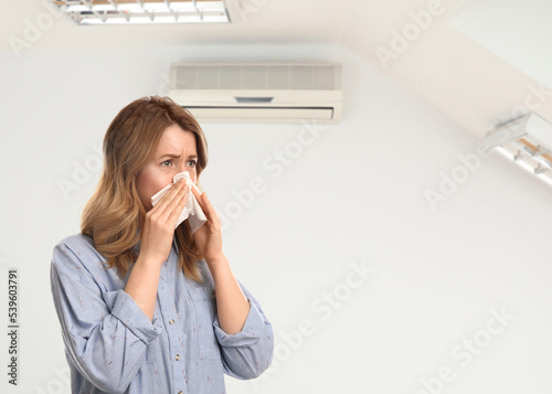 Obraz na płótnie Woman suffering from cold in room with air conditioner on white wall