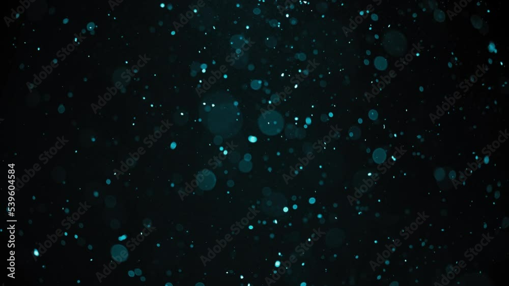Turquoise colored dust bokeh particles floating in the air. Slow motion. 