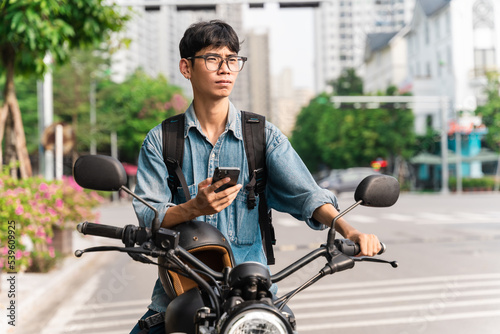 image of asian man, sitting on moto using mobile phone