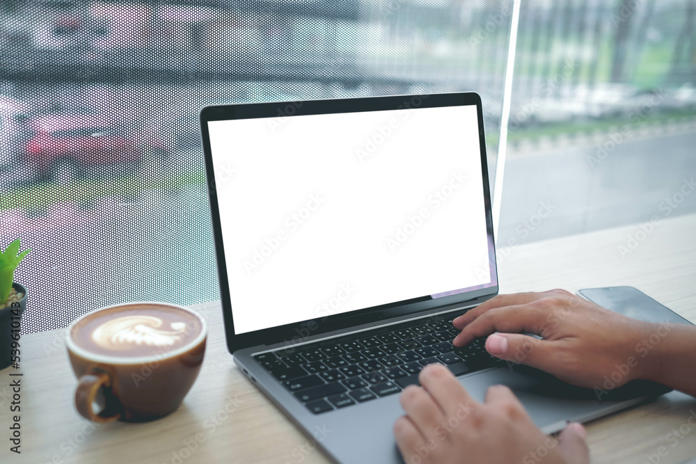 Mockup image of a businesswoman using laptop with blank white desktop screen with coffee cup on wooden table in cafe. Mockup image of a businesswoman using laptop with blank white desktop screen with coffee cup on wooden table in cafe.