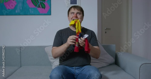 Sick man has strange addiction to socks eating clothes in room. Brown-haired guy with red runny nose happy to find lost clothes chewing socks