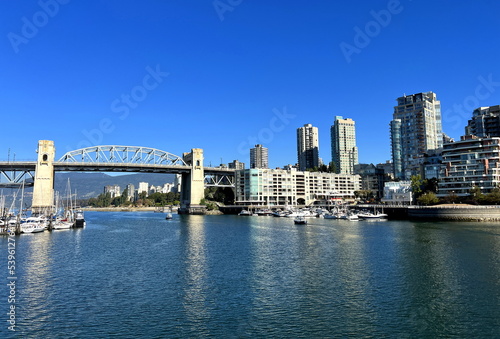 Bridge to greenville and water bus passing under the bridge Nature Canada Vancouver Pacific Ocean Pier and pillars on the pier Granville Island aquabus Skyscrapers in the background 09.2022 Canada © Oleksandra