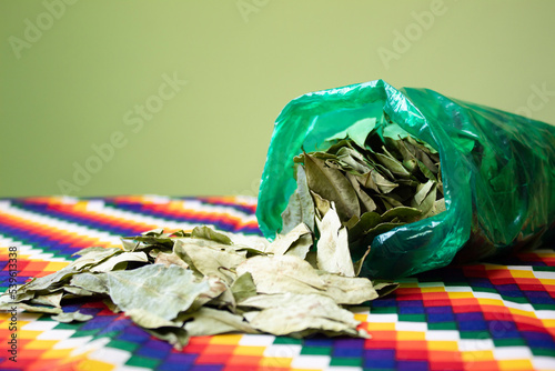 Coca leaves on table, Aymara and Inca indigenous cloth. Traditional use of coca in the Andean zone, valleys and tropics of Bolivia, Peru. tcolors of the tahuantinsuyo whipala photo