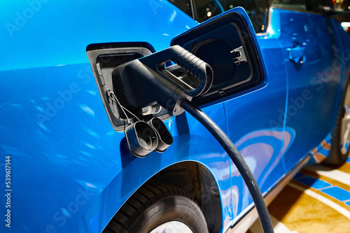 Charging electric blue automobile with plug at power station