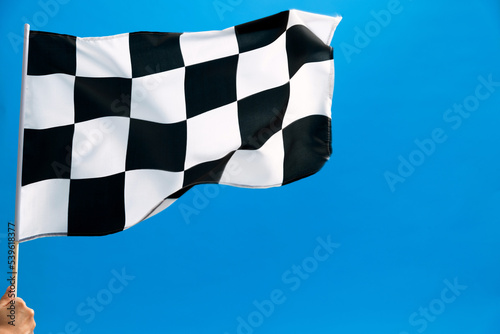 Human hand waving checkered flag on blue background